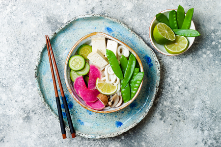 Vegan asian udon noodles soup bowl with ginger and mushrooms broth, tofu, snap peas, zucchini, watermelon radish and lime.の写真素材
