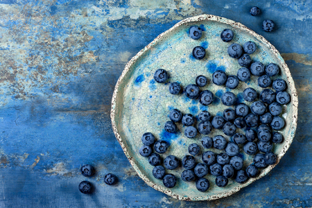 Fresh blueberries on the vintage ceramic plate over blue background. Top view, flat lay. Healthy eating concept.の写真素材