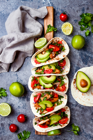 Mexican grilled chicken tacos with avocado, tomato, onion on rustic stone table. Recipe for Cinco de Mayo party. Top view, overhead, flat lay.の写真素材