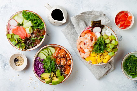 Hawaiian salmon, tuna and shrimp poke bowls with seaweed, avocado, mango, pickled ginger, sesame seeds. Top view, overhead, flat lay Hawaiian salmon, tuna and shrimp poke bowls with seaweed, avocado, mango, pickled ginger, sesame seeds. Top view, overhead, flat lay