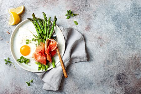 Green asparagus with fried egg, fresh oregano leaves and prosciutto on the plate. Top view.の写真素材