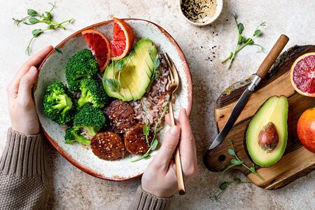 Girl holding Vegan tempeh buddha bowl. Marinated tempeh in smoky bbq sauce marinade or teryaki tempeh with rice, steamed broccoli, avocado, blood orange and micro greens.の写真素材