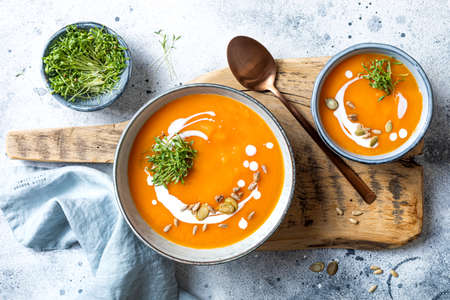 Vegetarian autumn pumpkin and carrot soup with cream, seeds and cilantro micro greens. Comfort food, fall and winter healthy slow food conceptの写真素材