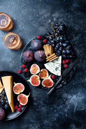 Appetizers, antipasti snacks and wine in glasses. Cheese and fruit platter on marble board over...