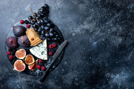 Appetizers, antipasti snacks and wine in glasses. Cheese and fruit platter on marble board over black background. Top viewの写真素材