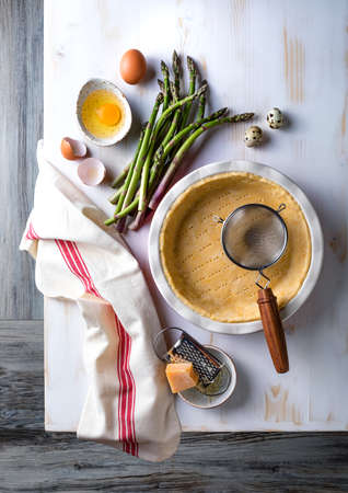 Cooking green asparagus, sweet peas Tart. Seasonal spring dinner baking with asparagus. Kitchen table, overhead view.の写真素材