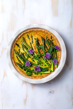 Green asparagus, sweet peas Tart with edible chives flowers or blossoms. Seasonal spring dinner, overhead view.の写真素材