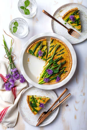 Green asparagus, sweet peas Tart with edible chives flowers or blossoms. Seasonal spring dinner table, overhead view.の写真素材