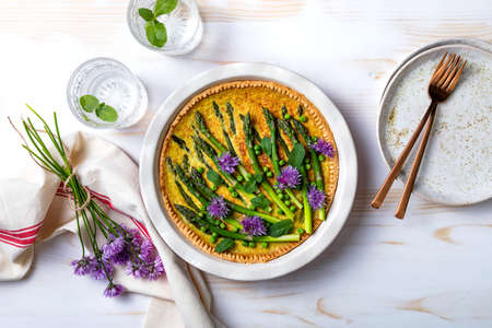 Green asparagus, sweet peas Tart with edible chives flowers or blossoms. Seasonal spring dinner table, overhead view.の写真素材