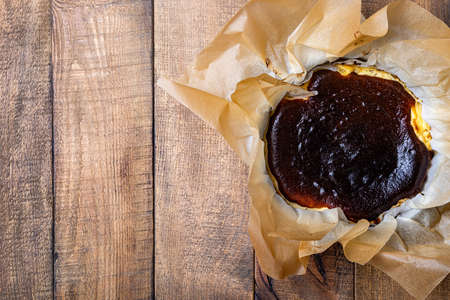 San Sebastian Basque Burnt Cheesecake. Basque burnt cheesecake on baking paper over wooden background. top viewの写真素材