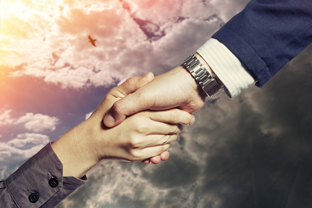 Photo which shows a handshake of two persons, on a sky background with a flying birdの写真素材