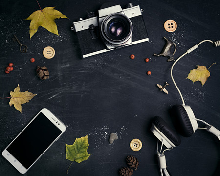 Composition of suede shoes, retro camera, headphones, mobile, yellow leaves on a dark, scratched background.  In the center of the free space for your design. Mock up for art work.の写真素材