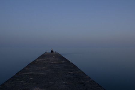 young girl sitting on the edge of the pier in the lotus position, she breathes the sea air and enjoy the silenceの写真素材