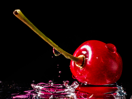 Close up of fresh cherry berrie with water drops and splash on black backgroundの写真素材