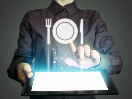Image of a girl with tablet in her hands and food restaurant icon. She looking menus, ordering food delivery, rate restaurant with using online services.の写真素材