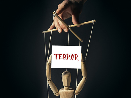 Tiran holds a puppet on strings, in doll's hands a  banner with inscription "terror".  Image on black background.の写真素材
