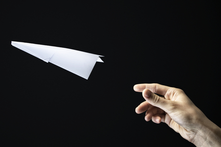 Image of a hand is throwing  white paper plane on black background.の写真素材