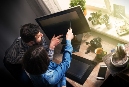 Teamwork, cooperation, assistance. Workflow of designers. Employees (male and female) discuss the project sitting at the desk.の写真素材