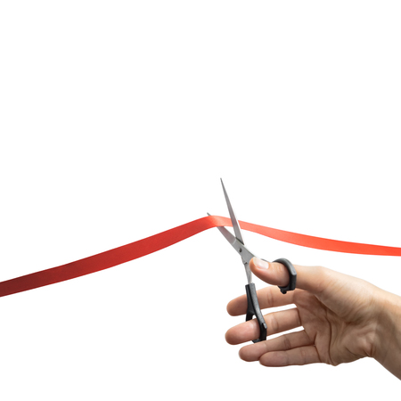 The concept of the grand opening of something. Scissors in female hands cuts the red satin ribbon.の写真素材