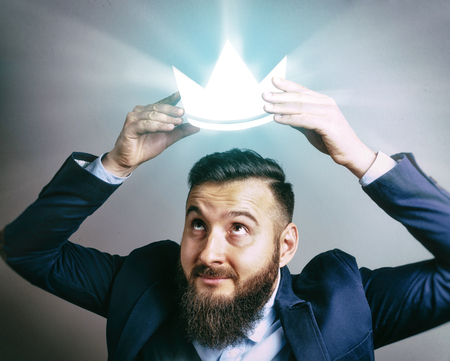 The image of a man in a suit that puts a luminous royal crown on his head. The concept of careerism, achieving the goal, smugness, egoism, success and etc.の写真素材