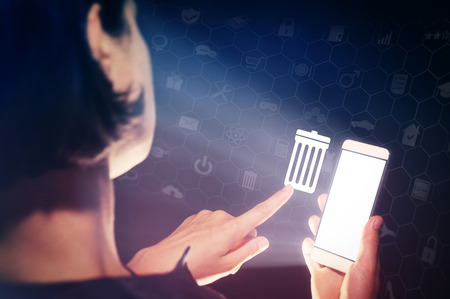 Image of a girl with a smartphone in hands. She presses on the trash can icon. The concept of...