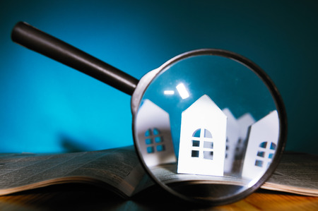 Magnifying glass in front of an open newspaper with paper houses. Concept of rent, search, purchase real estate.の写真素材