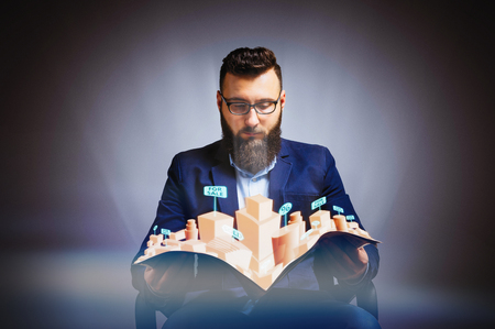 Man holds a newspaper in his hands. Newspaper has a hologram with real estate for sale. Concept of online realtor.の写真素材