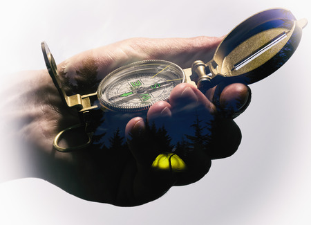 Man's hand with a compass. Double exposure, beautiful landscape background. Made in vintage style.の写真素材