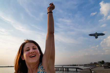 Happy young woman running with a kite on a beach at sunset in summer.