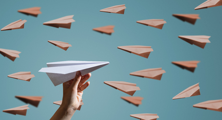 Hand launches a paper plane to towards other aircrafts on blue backgroundの写真素材