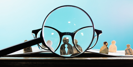 Business recruitment or hiring photo concept. Looking for talent. Icons of candidates are standing on open newspaper under magnifier.の写真素材