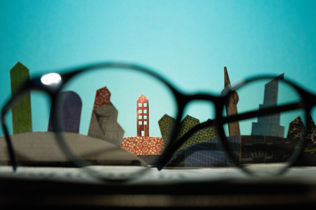 Glasses in front of an open newspaper with paper houses. The concept of renting, searching, buying real estate.の写真素材