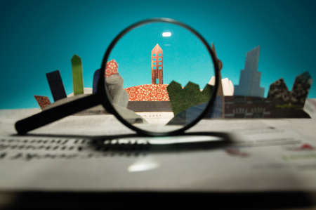 Magnifier in front of an open newspaper with paper houses. The concept of renting, searching, buying...