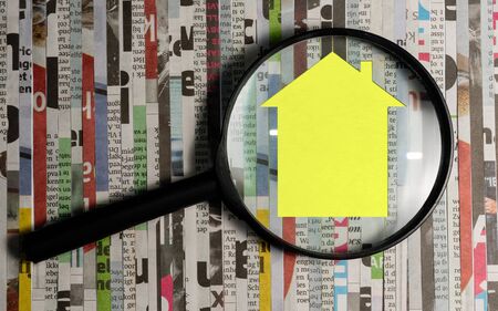 Magnifying glass in front of an open newspaper with paper houses. Concept of rent, search, purchase real estate.の写真素材