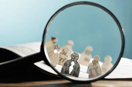 Business recruitment or hiring photo concept. Looking for talent. Icons of candidates are standing on open newspaper under magnifier.の写真素材
