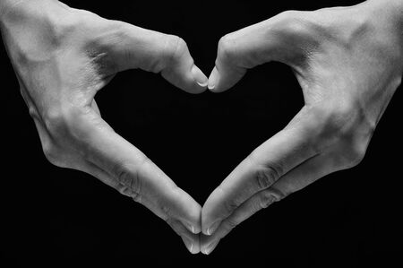 Two hands in the shape of a heart on black isolated background. The concept of love, harmony, caring.の写真素材