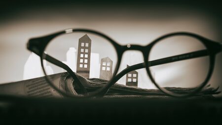 Magnifying glass in front of an open newspaper with paper houses. Concept of rent, search, purchase real estate.の写真素材