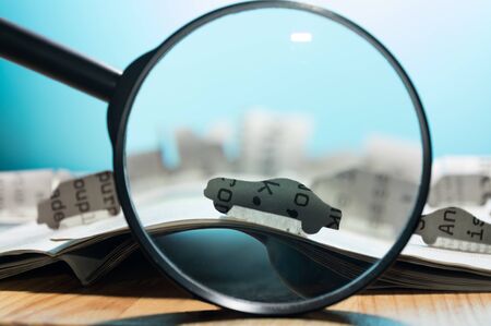 Magnifying glass in front of an open newspaper with paper cars. Concept of car rent, search,...