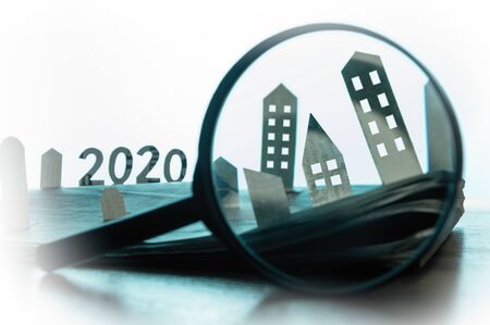 Magnifying glass in front of an open newspaper with paper houses. Concept of rent, search, purchase...