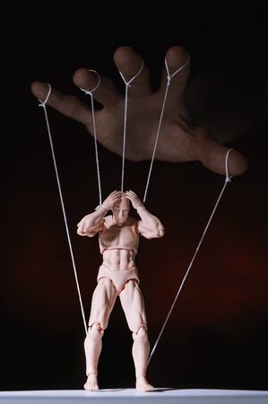 Concept of control. Marionette in human hand. Objects are colored on red and blue light.の写真素材