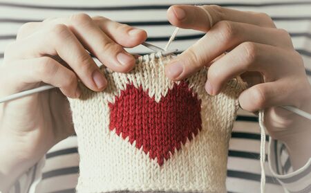 Concept of love and concern. Woman knitting the red heart for her loved one. Valentines postcard.の写真素材
