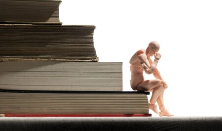 Puppet of human is sitting on stack of books. Concept of learning.