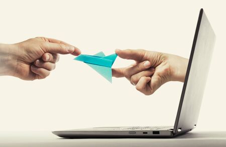 Person gives paper plane to another human via laptop. Concept of booking plane ticket, charters, tour.の写真素材