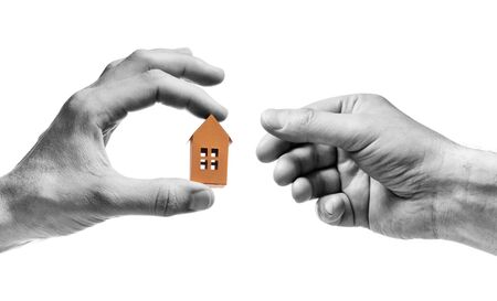 Man's hand reach out to paper house in the palm of woman hand. Concept of rent, search, purchase real estate. Black and white. Isolated on white.の写真素材