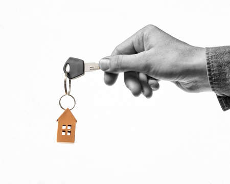 Key with orange paper house in human hand. Concept of rent, search, purchase real estate. Black and...