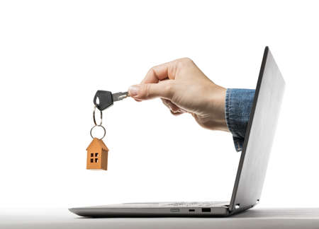 Key with paper house in human hand stick out of a laptop screen. Concept of modern technologies in...