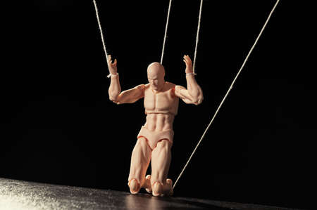 Concept of control. Marionette on his knees on black background.の写真素材