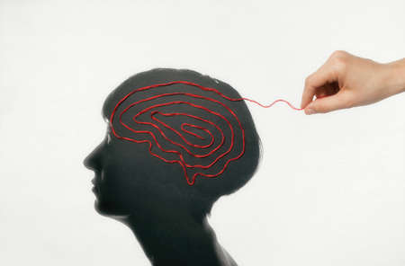 The woman hand pulls on the thread laid out in the shape of a brain in woman head. Concept of...
