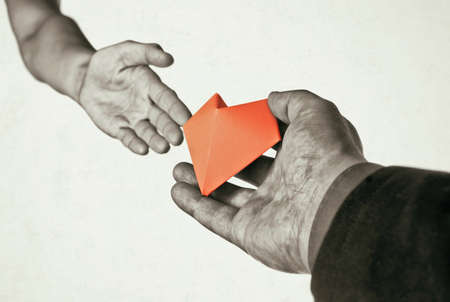 Red heart in woman and man hands. Concept of love, giving gifts, donorship. Black and white.の写真素材