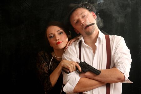 Portrait of the man in a hat with a cigar and a pistol and the beautiful woman. In style of a retro.の写真素材